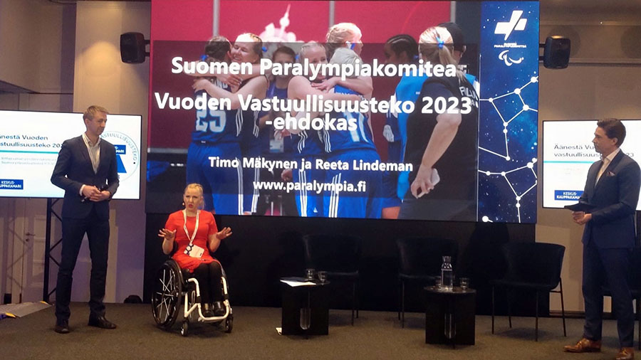 Reeta Lindeman ja Timo Mäkynen puhumassa yleisölle. Taustalla screeni, jossa: Suomen Paralympiakomitea Vuoden Vastuullisuusteko 2023 -ehdokas.